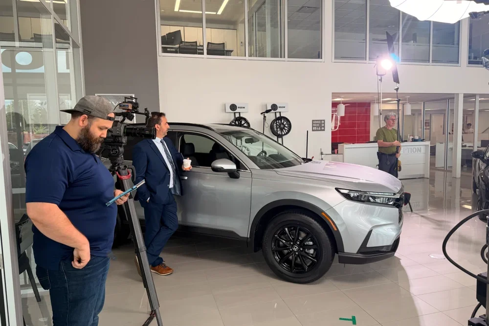 A cameraman filming a grey Honda SUV at the dealership for the Fidgi video