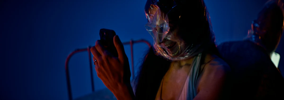 Image du vidéoclip Wicked Signal : femme au visage recouvert de plastique regardant son téléphone
